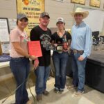 Three people holding a trophy and a bottle.