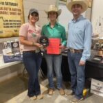 Three people stand smiling, holding awards.