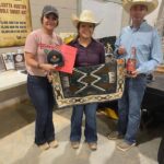 Three people holding a rug and a bottle of whiskey.